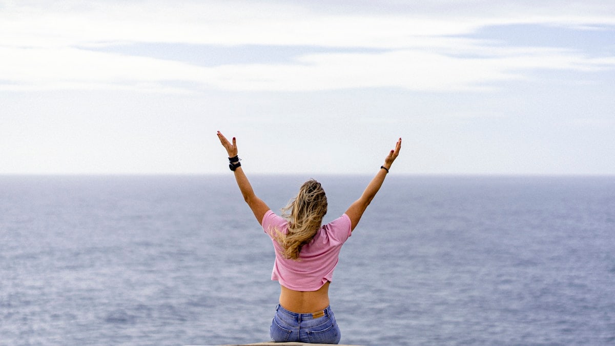 a woman with her arms raised in front of a body of water